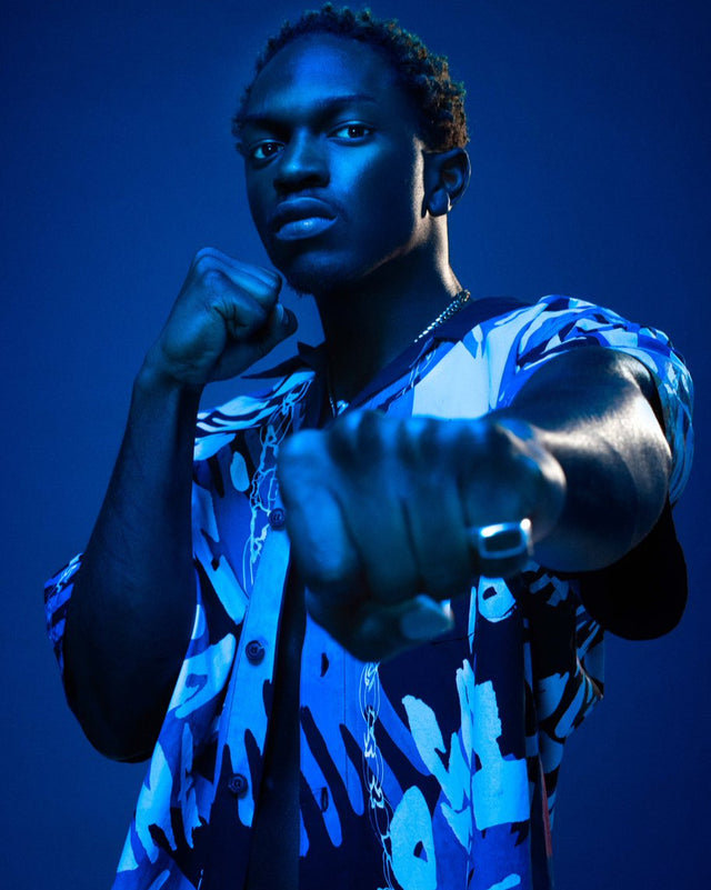 Kida Kudz wearing a blue patterned outfit and an inlaid oxford ring with onyx with a dark blue background